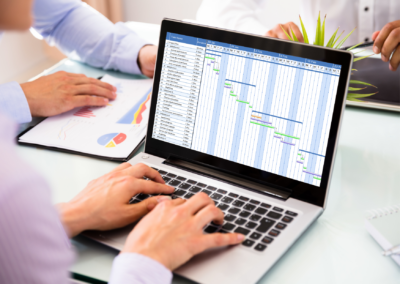Team reviewing a project Gantt chart on a laptop during a planning meeting, illustrating an energy project leadership and coordination project